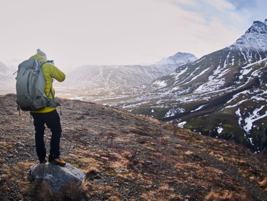 A male wearing a yellow jacket and a backpack while taking a picture of the beautiful scenery
